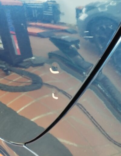Dunkle Fahrzeugtür mit kleiner Delle im Spiegelbild der Werkstatt