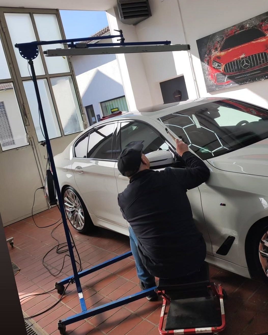 Techniker bei der lackschadenfreien Dellenentfernung an einer weißen Limousine unter einer Prüflampe