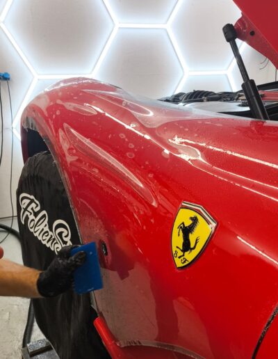 Steinschutzfolie wird an der Seitenpartie eines roten Ferrari aufgerakelt